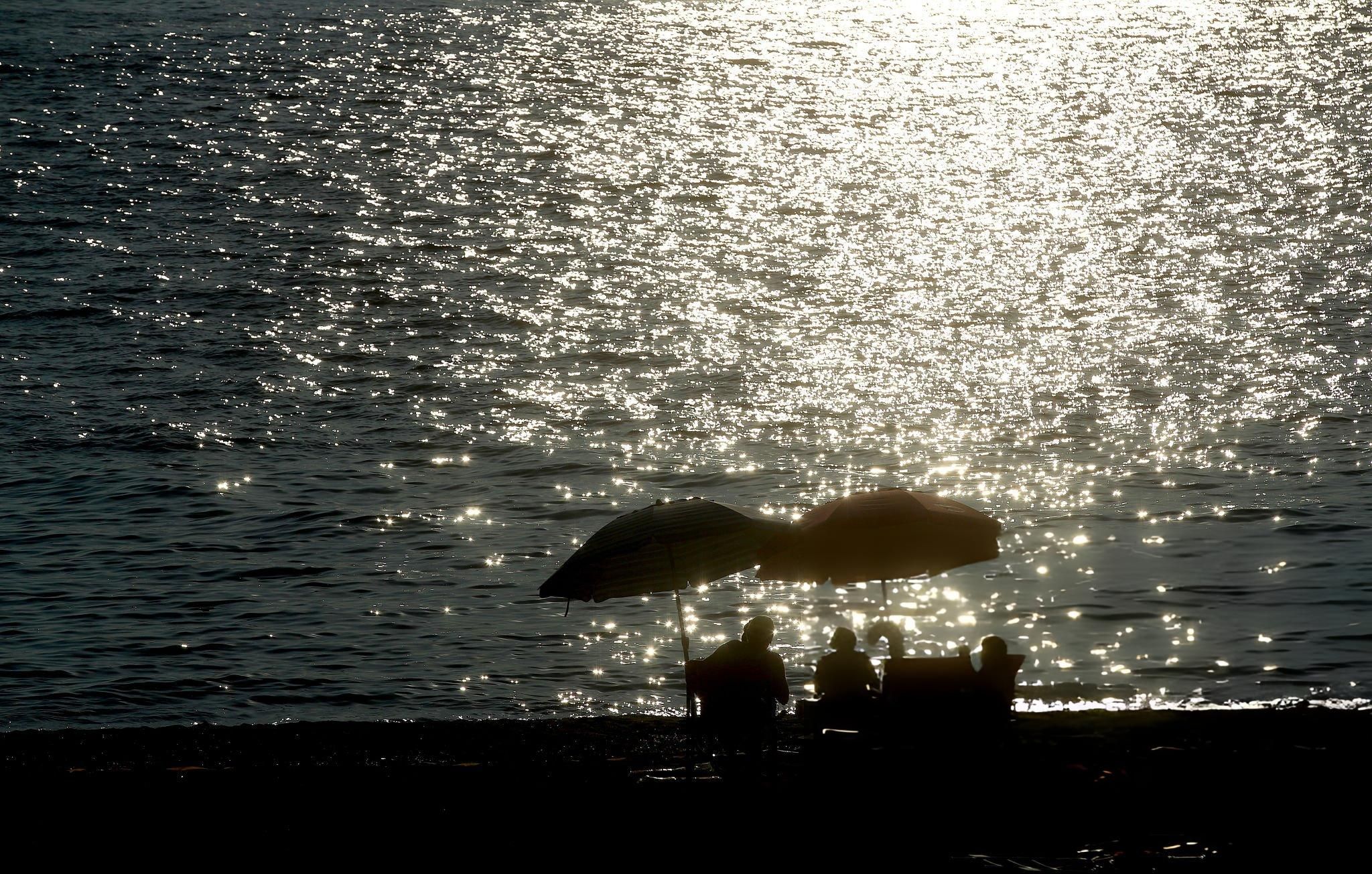 Silhouetted couple sitting under umbrellas by the ocean during golden sunset on a Vancouver beach.