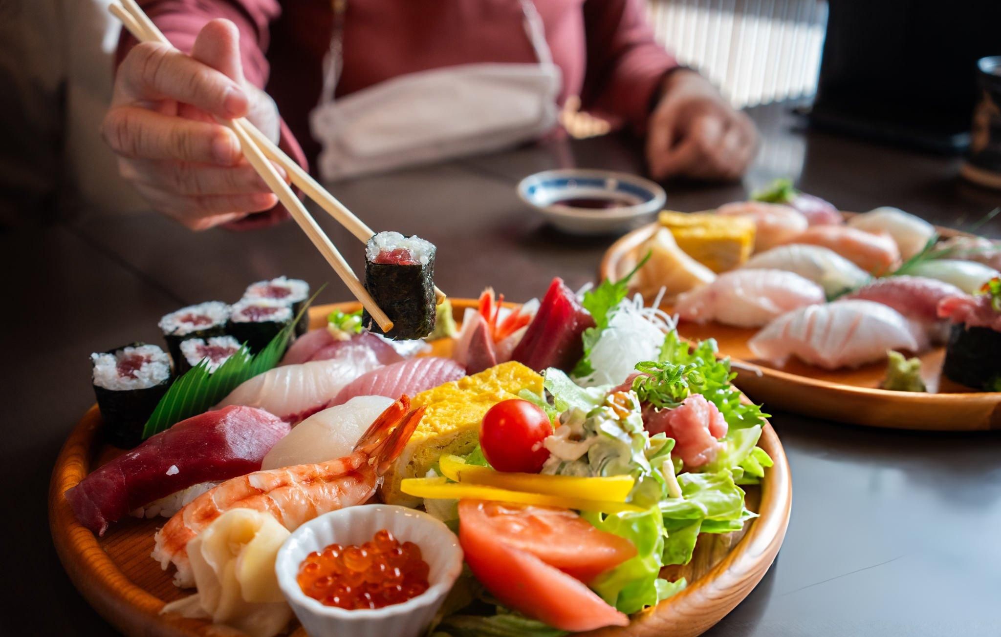 People eating freshly prepared sushi with side dishes 